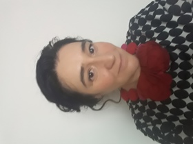 Dr Penades in front of a white wall wearing a black and white top with red necklace