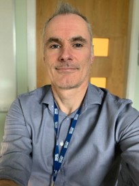 Dr Anderson posing in an office seeting wearing a blue shirt and NHS lanyard